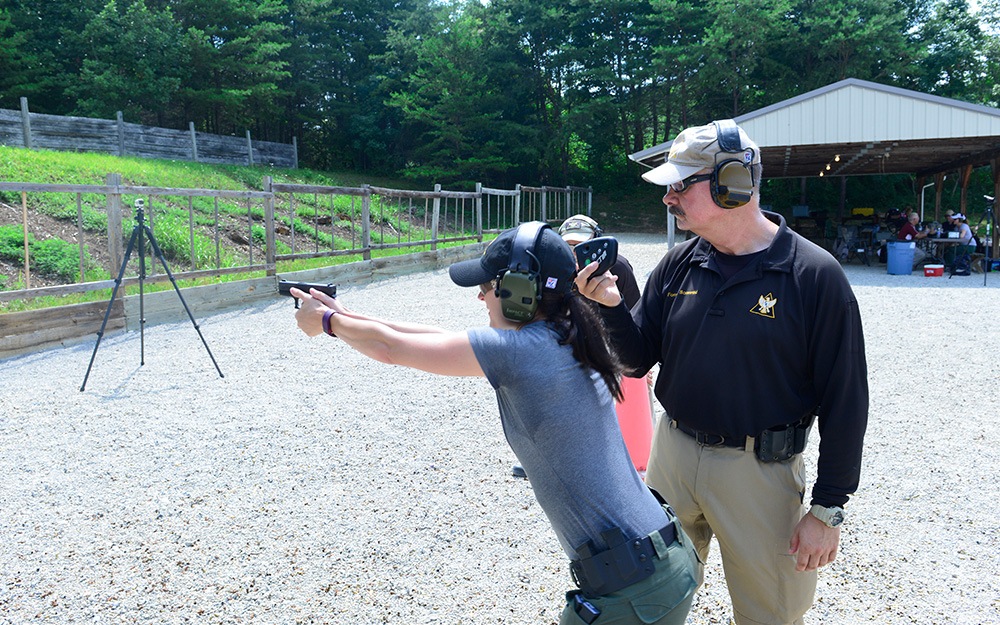 A veteran male training a middle-aged woman how to properly stand and aim her gun at a target.